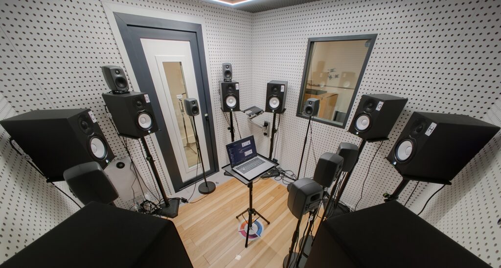 A DXOMARK audio laboratory showing a laptop being evaluated for audio conference sound quality, surrounded by numerous speakers reproducing the ambient noise of a conference call.